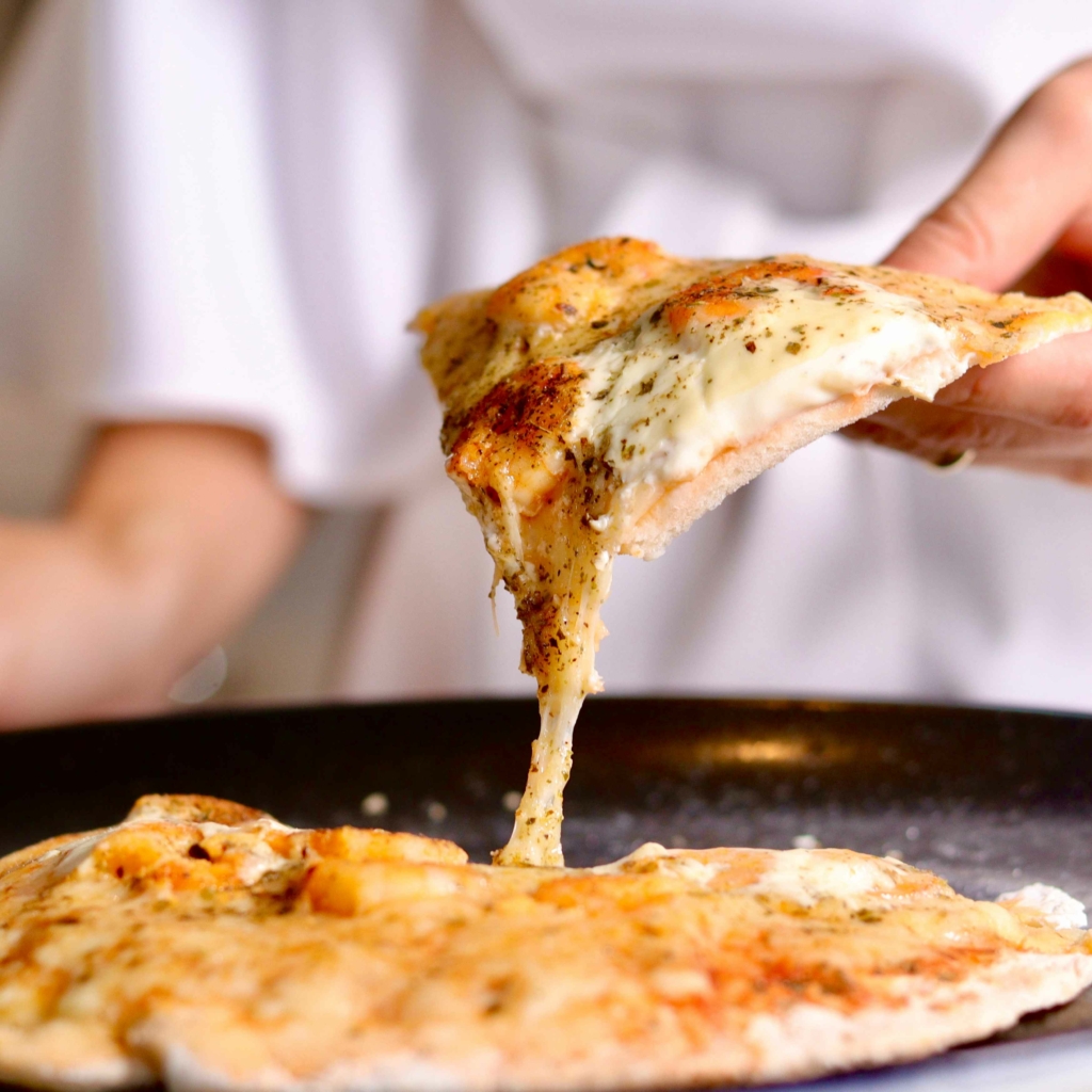 mani che  prendono una fetta di pizza sottile e con cornicione basso