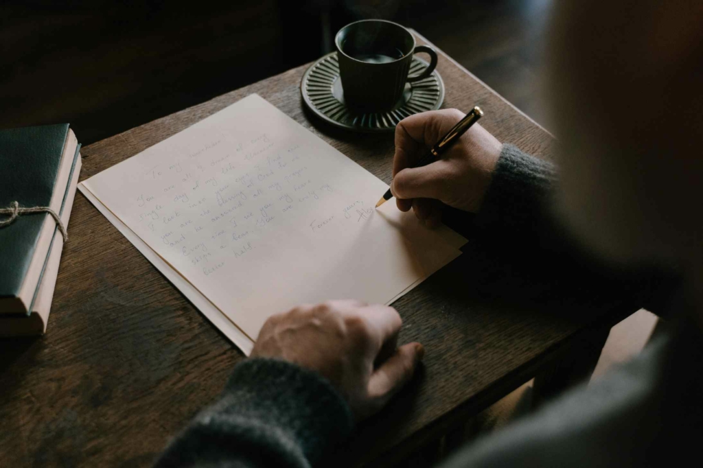 uomo che  scrive al atavolino di un bar con accanto una tazza di caffè