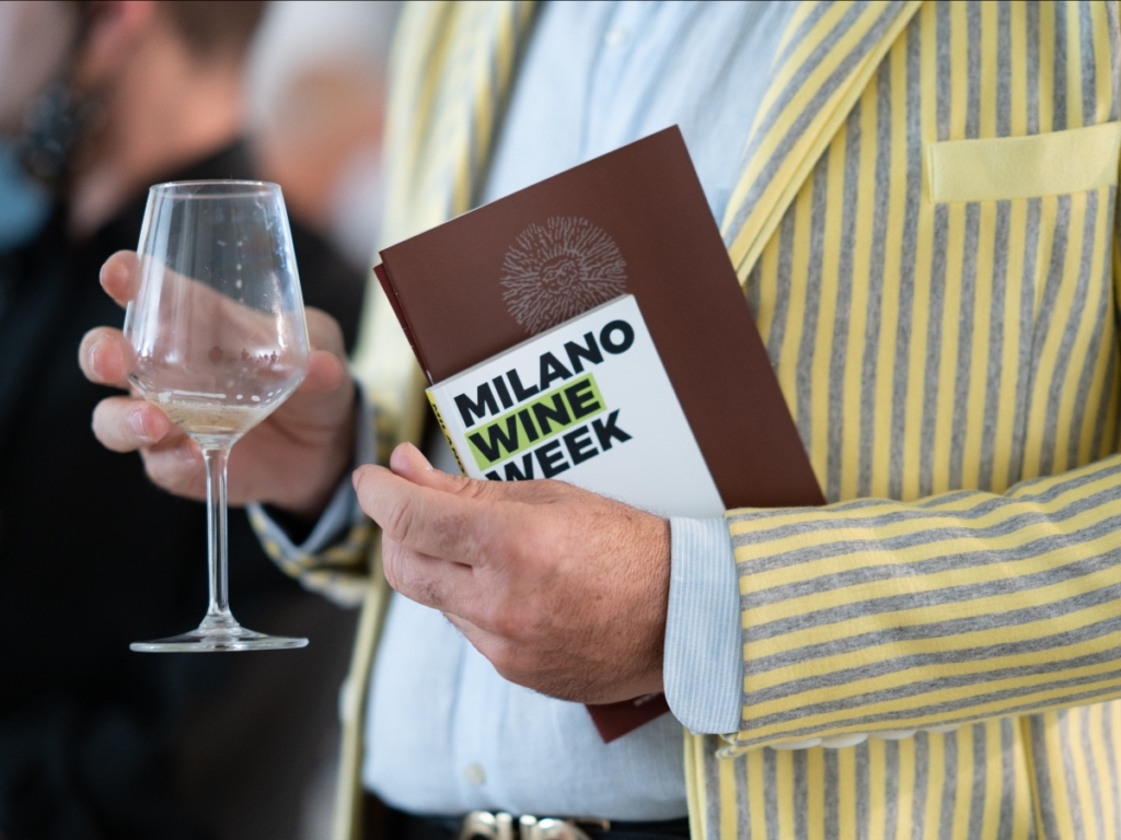 Una persona del pubblico della Milano Wine Week con in mano la brochure dell'evento e un calice di vino