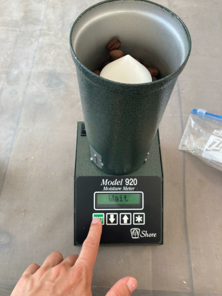 operatore della farm che preme il dito sul tasto "test" del macchinario, per effettuare il controllo dell'umidità delle drupe di caffè, che se raggiungono l'11% possono essere tolte dalla stanza di essicazione.